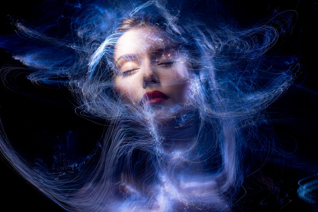 Abstract portrait of a woman with swirling blue light trails and closed eyes.