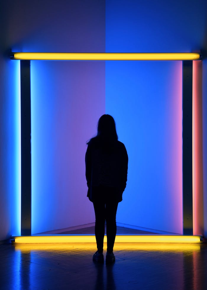 A woman stands silhouetted against vibrant neon lights, creating a colorful visual impact.